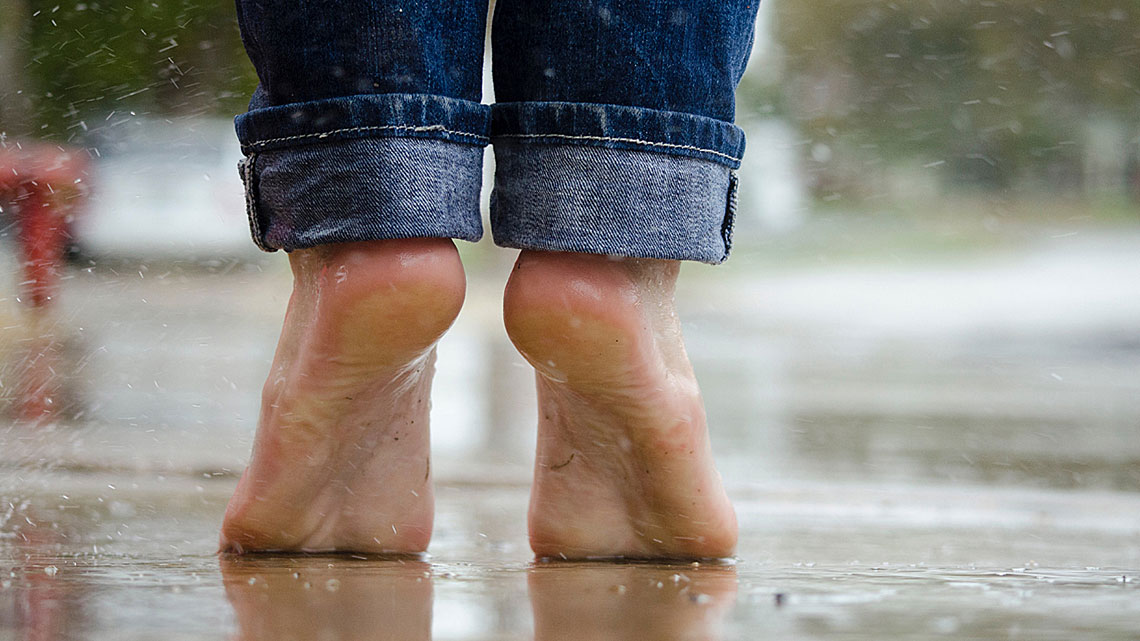 Zwei nackte Füße auf Zehenspitzen auf dem Boden, der vom Regen nass ist. 