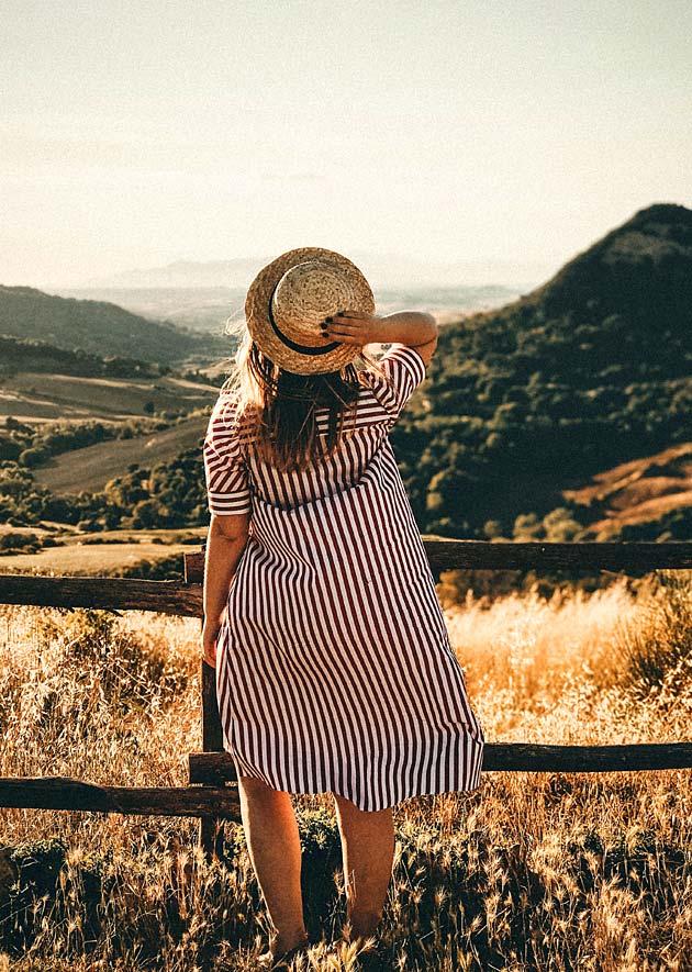 Frau im Sommerkleid genießt die Aussicht auf die Felder und Berge.
