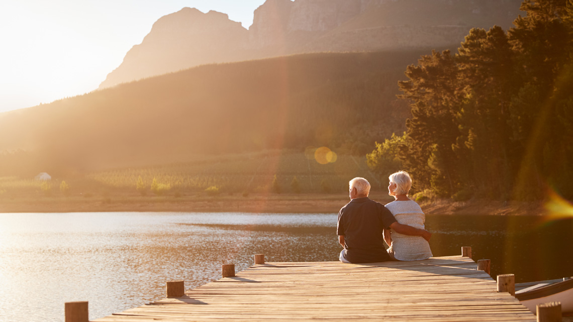 Sitzendes Rentnerpaar am Steg mit Blick auf den See.