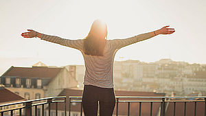 Frau von hinten, die die Arme ausstreckt und die Aussicht auf ihrem Balkon genießt. | © pixabay.de