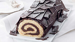 Kuchen in Form eines Weihnachtsbaumstamms mit Puderzucker bestäubt. | © StockFood
