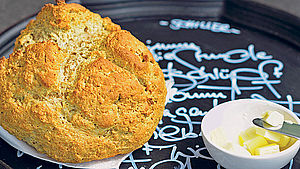 Runder, heller Brotlaib mit einem Schüsselchen Butter auf einem Tablett. | © Jutta Schneider / Michael Will
