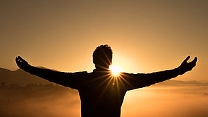 Mann, der im Sonnenuntergang auf einem Berg steht und die Arme ausbreitet | © Zac Durant, unspalsh.com