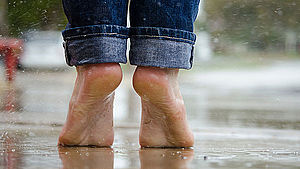 Zwei nackte Füße auf Zehenspitzen auf dem Boden, der vom Regen nass ist. 