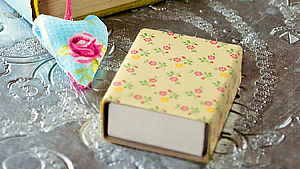 Genähtes Lesezeichen in Herzform neben einer mit Blumenstoff beklebten Streichholzschachtel. | © Tanja Westendorf