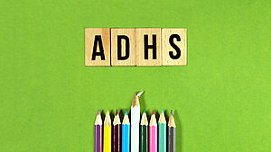Schriftzug ADHS mit bunten Holzstiften im Bild auf grünem Hintergrund. | © shutterstock.com