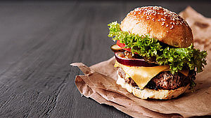Frischer, hausgemachter Cheesburger auf Backpapier auf einem Holztisch. | © Mikhaylovskiy/shutterstock.com