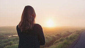 Frau von hinten, dieden Sonnenaufgang betrachtet. | © shutterstock.com