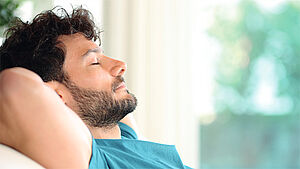 Mann, der sich mit geschlossenen Augen entspannt zurücklehnt. | © Vladiri/Shutterstock