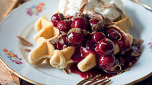 Teller mit selbstgebackenen Waffeln, Kirschkompott und Sahne. | © Andrea Natschke-Hofmann