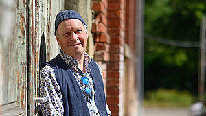 Rainer Haak lehnt mit Rücken an der Wand einer alten Holztür. | © Stefan Weigand