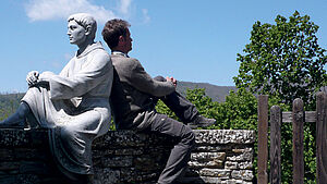Jörn Heller sitzt auf einer Mauer Rücken an Rücken mit einer Steinfigur. | © privat