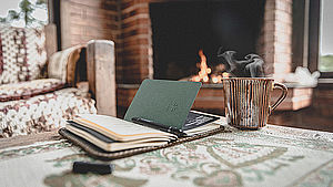 Terminkalender und Kaffeetasse auf Tisch, im Hintergrund Kachelofen. | © Rafael Leão, unsplash.com