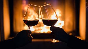 Anstoßen mit zwei Gläsern Wein mit Kamin im Hintergrund. | © Denis Kalinichenko, Shutterstock.com