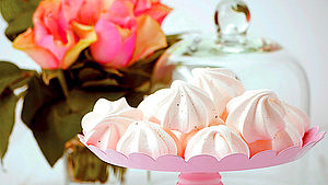 Meringues in einer rosafarbenen Schale, im Hintergrund Rosenstrauß. | © Lorthios/Photocuisine 