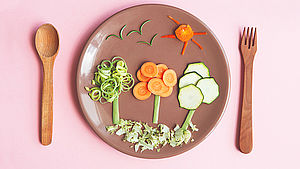 Teller mit rohem Gemüse als Bäume gelegt und Holzbesteck auf rosa Hintergrund. | © Alina Kruk, shutterstock.com