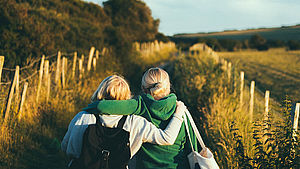 Rückansicht zweier Frauen, die Arm in Arm auf einem Feldweg spazieren gehen. | © Joseph Pearson, unsplash.com