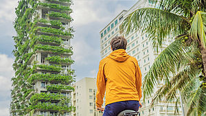 Mann auf einem Fahrrad steht vor Gebäude mit grün beplfanzter Hauswand | © shutterstock.com/Elizaveta Galitckaia