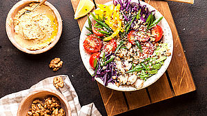 Teller mit angerichtetem Salat auf Holzbrett, daneben in 2 Schüsselchen Aufstrich und Walnüsse. | © Mariana Medvedeva/Unsplash