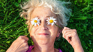 Ältere Frau liegend auf einer Wiese mit Gänseblümchen vor den Augen | Alonafoto / shutterstock.com