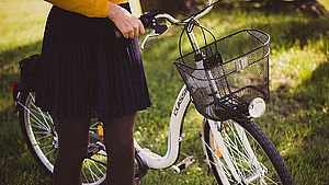 Frau steht in der Wiese und hält ihr Fahhrad am Lenker fest.