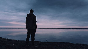 Silhouette eines Mannes, der an einem See steht. | © unsplash.com