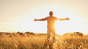 Mann von hinten mit ausgestreckten Armen gegen die Sonne. | © shutterstock.com