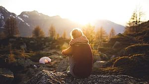 Frau sitzend in der Natur, mit Blick auf ihr Zelt. Im Hintergrund Berge. | © StockSnap, pixabay.com