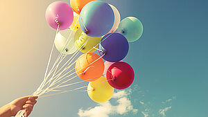 Bunte Luftballons an Schnüren in einer Hand. Hintergrund Himmel. | © shutterstock.com